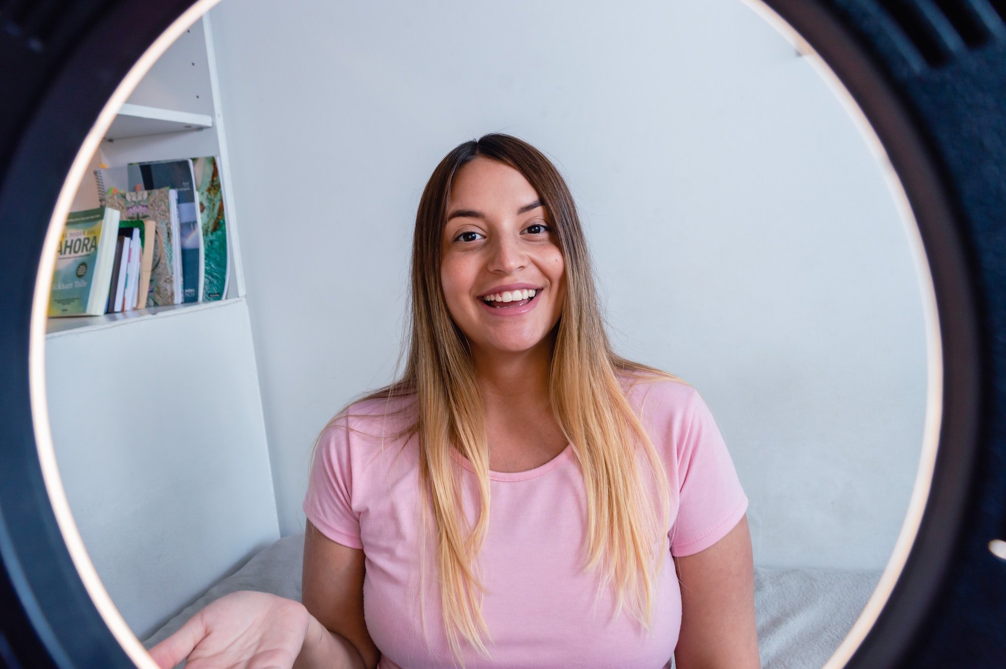 portrait through ring of light of young woman generating content, smiling looking at the camera