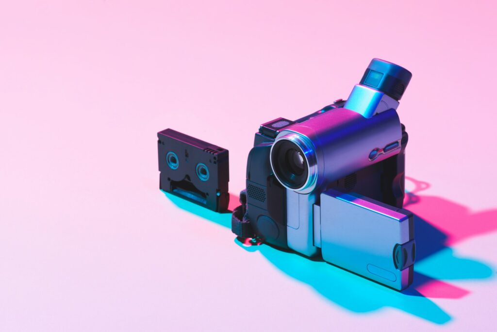 close up view of video cassette and digital video camera on pink background