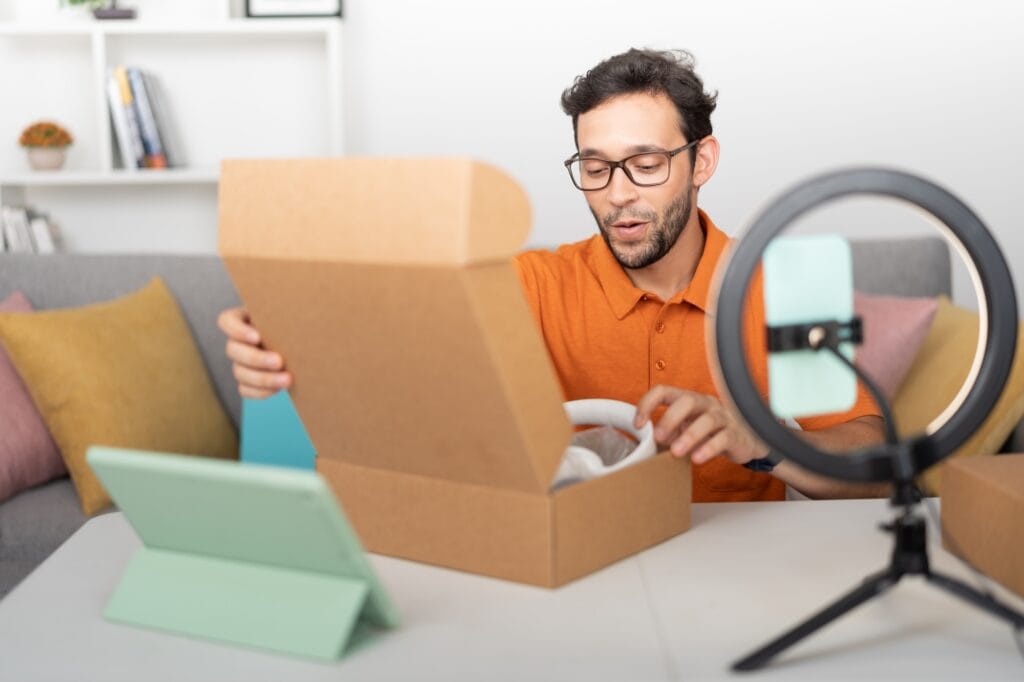 Male influencer sitting at a desk, recording a video while unboxing a gift.